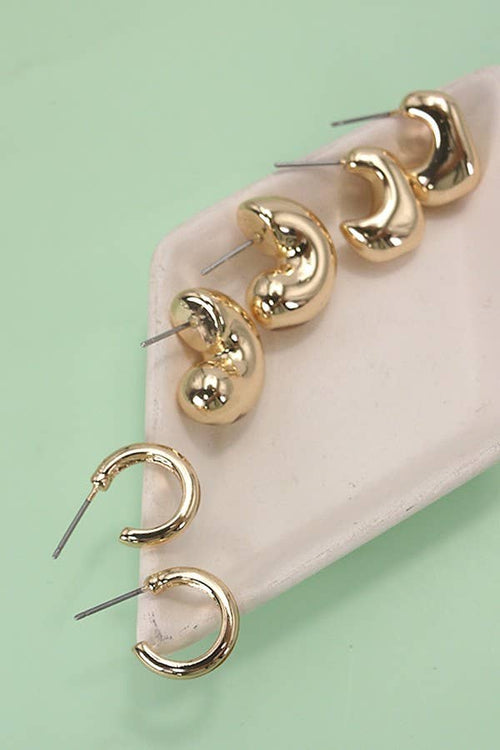 Gold hoop earrings on a pink stand against a light green background
