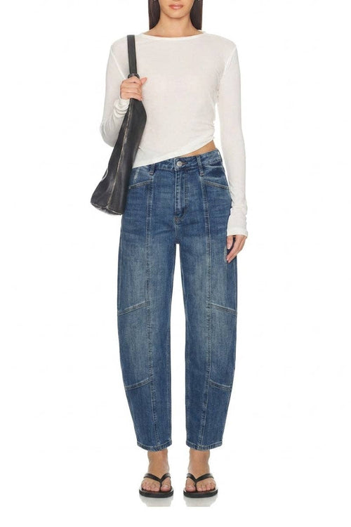 A model wearing a white long-sleeve crop top, blue wide-leg cropped jeans with patch pockets, and black sandals, holding a black shoulder bag against a white background.