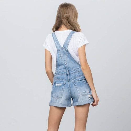 Person wearing light blue denim overalls and white sneakers on a plain background