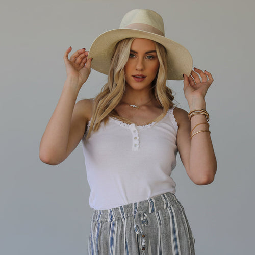 Woman wearing a wide-brimmed hat, white top, and striped pants 