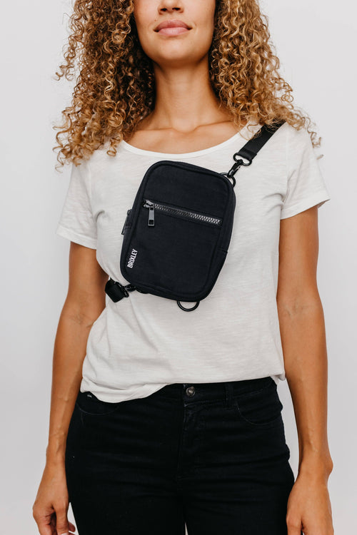 Person wearing a black crossbody bag on a plain background