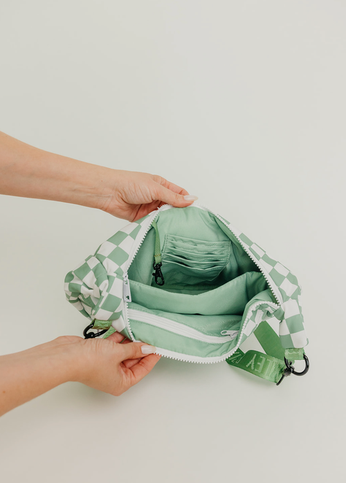 Green and white checkered bag being held open by a person on a light background