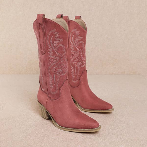 Pair of pink cowboy boots with intricate white stitching on a beige background
