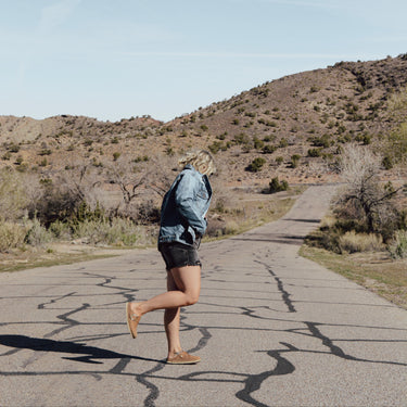 Person walking on a paved road in a desert landscape with mountains in the background