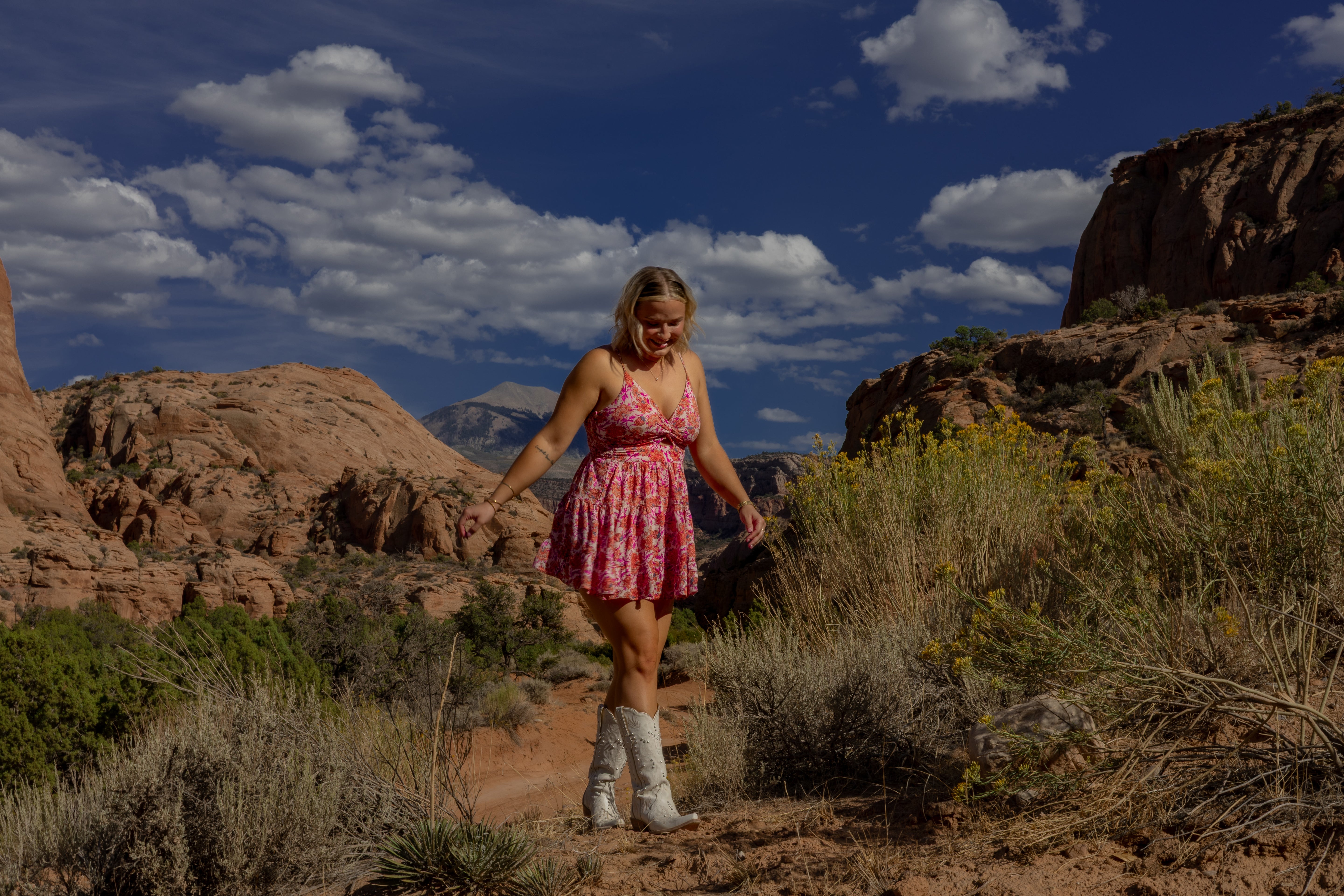 Woman in a pink dress standing in a desert landscape with rocky formations and blue sky.