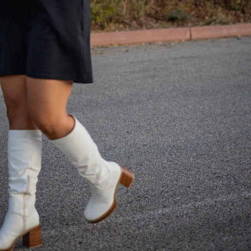 Person wearing a black dress with a graphic design, white knee-high boots, and checkered sleeves outdoors.