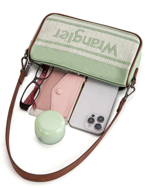 A mint green and white woven crossbody bag with brown leather trim and strap, shown open with a phone, card holder, glasses, and small round container inside. The bag has the Wrangler logo printed across the top on a white background.