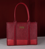 A red leather tote bag with a crocodile-embossed bottom panel and a gold-tone brand plaque, photographed against a dark red background.