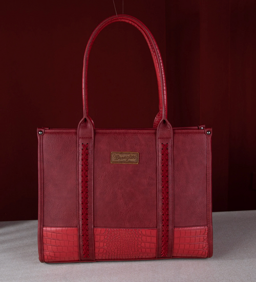 A red leather tote bag with a crocodile-embossed bottom panel and a gold-tone brand plaque, photographed against a dark red background.