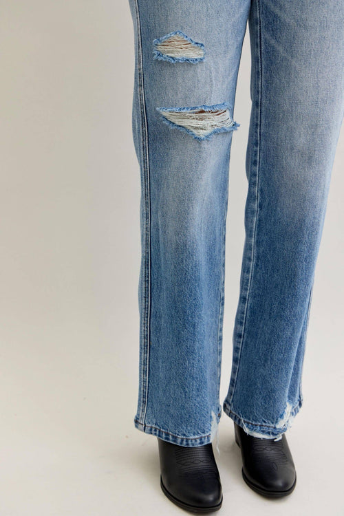 Ripped blue jeans worn by a person on a white background