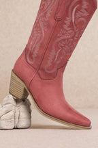 Pink cowboy boot with detailed stitching on a beige background