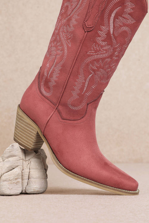 Pink cowboy boot with detailed stitching on a beige background