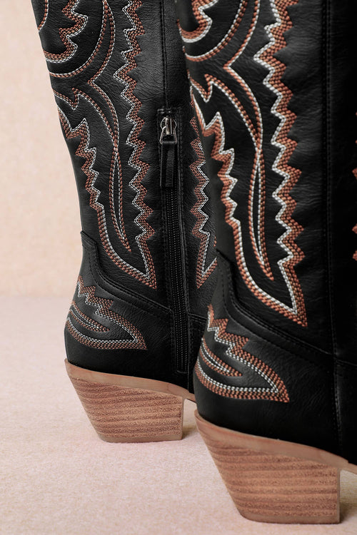 Black cowboy boot with intricate brown embroidery on a beige background