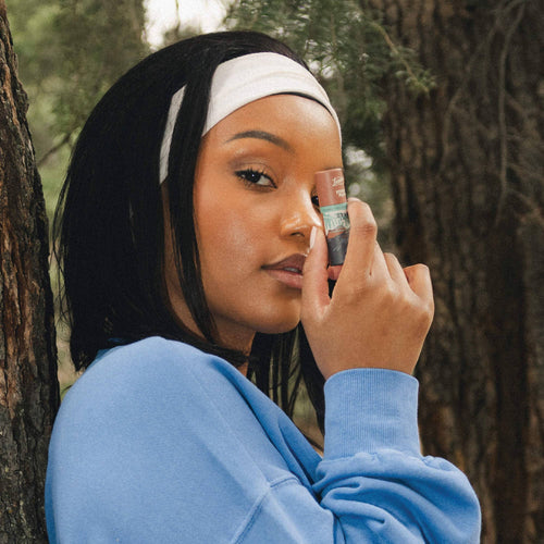 Woman applying lip balm outdoors with trees in the background