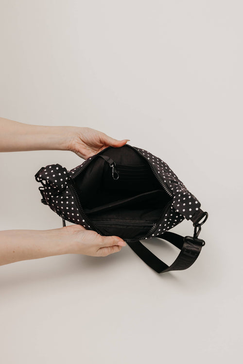 Black polka dot bag held by a person against a beige background