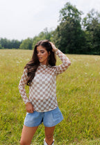 Woman wearing a checkered shirt and denim shorts standing in a grassy field.