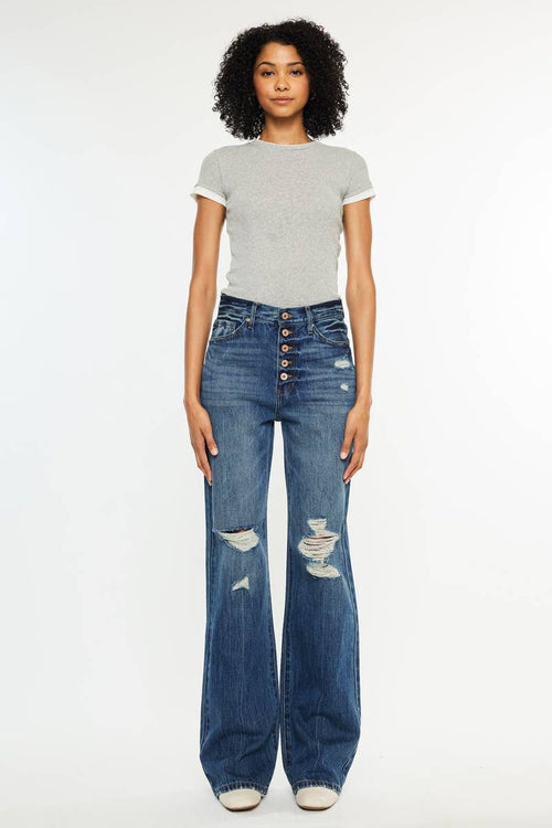 Woman wearing a gray t-shirt and blue jeans with button details on a white background
