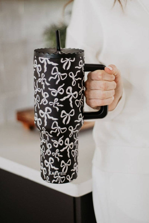 Black mug with white bow pattern held by a person in a blurred indoor setting