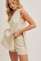 Woman wearing a beige sleeveless top and shorts on a plain background