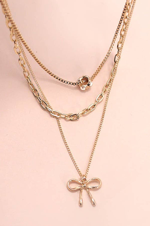 Gold chain necklaces with a bow pendant on a pink background