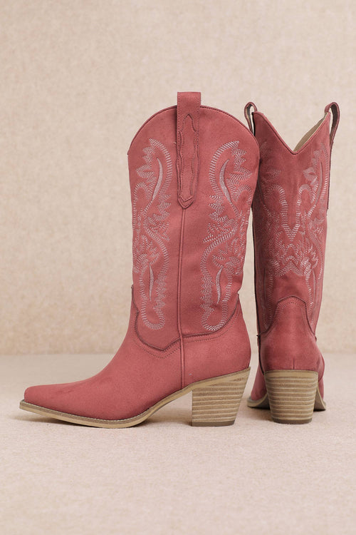 Pair of pink cowboy boots with intricate designs on a beige background
