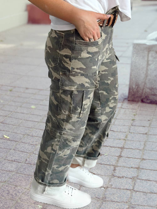Person wearing camouflage pants and white sneakers on a sidewalk.