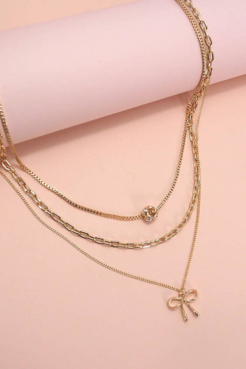 Gold necklaces with bow and ball pendants on a pink background