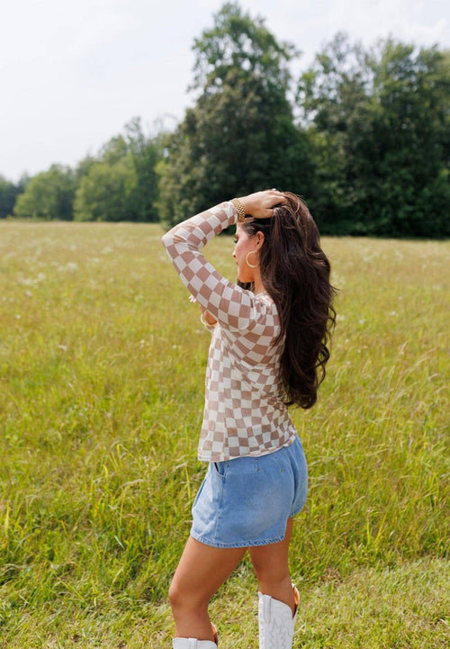 Woman in a checkered shirt and denim shorts standing in a field with trees in the background