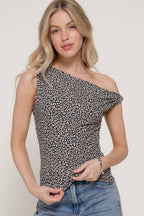 A woman modeling a one-shoulder sleeveless top with a black and white micro floral pattern, paired with blue jeans, against a plain light beige background.