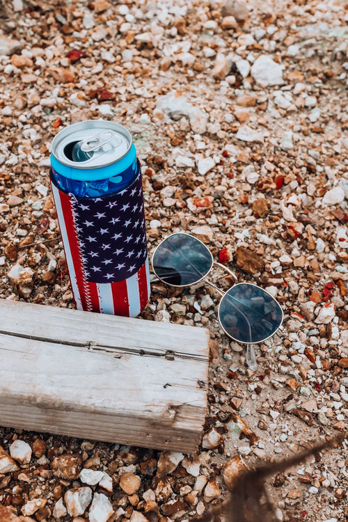 Cans with American flag design and sunglasses on a gravel surface