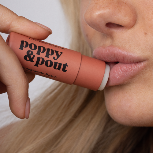 Person holding a 'poppy & pout' lip balm near their lips.