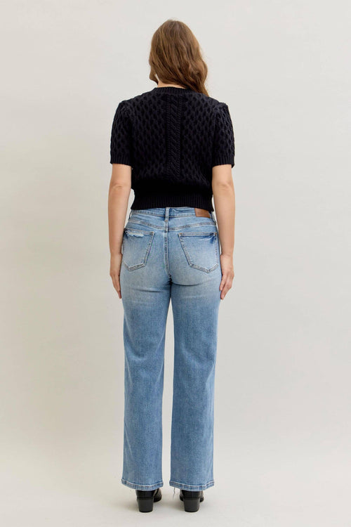Person wearing a black textured top and light blue jeans on a plain background