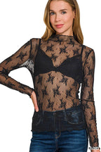 Woman wearing a sheer black lace top over a black bralette with blue jeans.