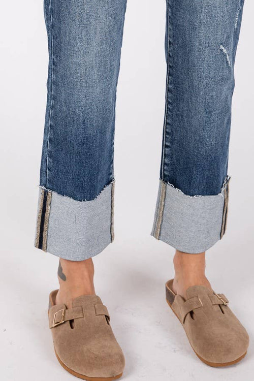 Cropped jeans with rolled-up hem and brown suede shoes on a white background