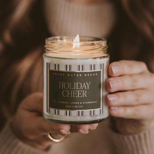 Person holding a 'Holiday Cheer' candle with a warm glow