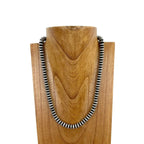 Necklace with silver beads on a wooden stand against a white background