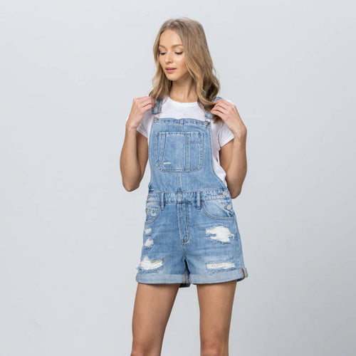 Woman wearing a denim overall romper with a plain background