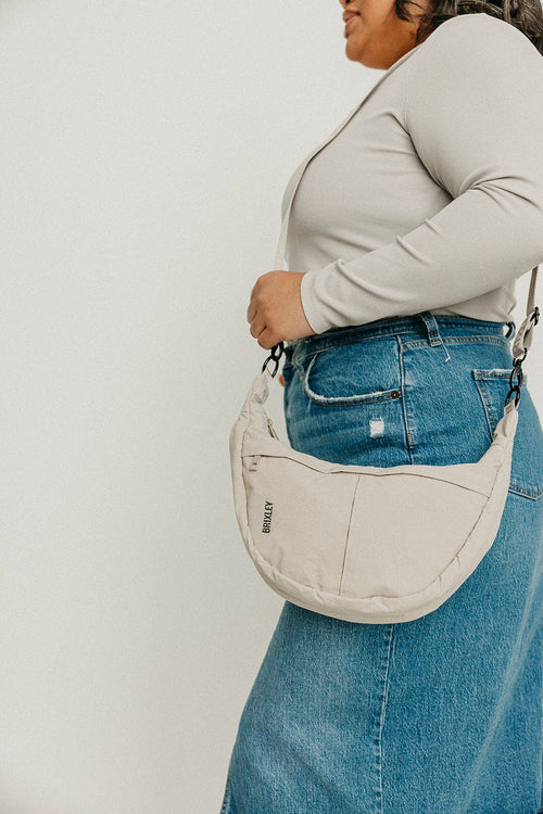 Person wearing a beige crossbody bag with a plain background