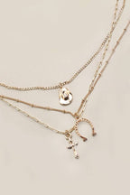Set of gold necklaces with various pendants on a light beige background
